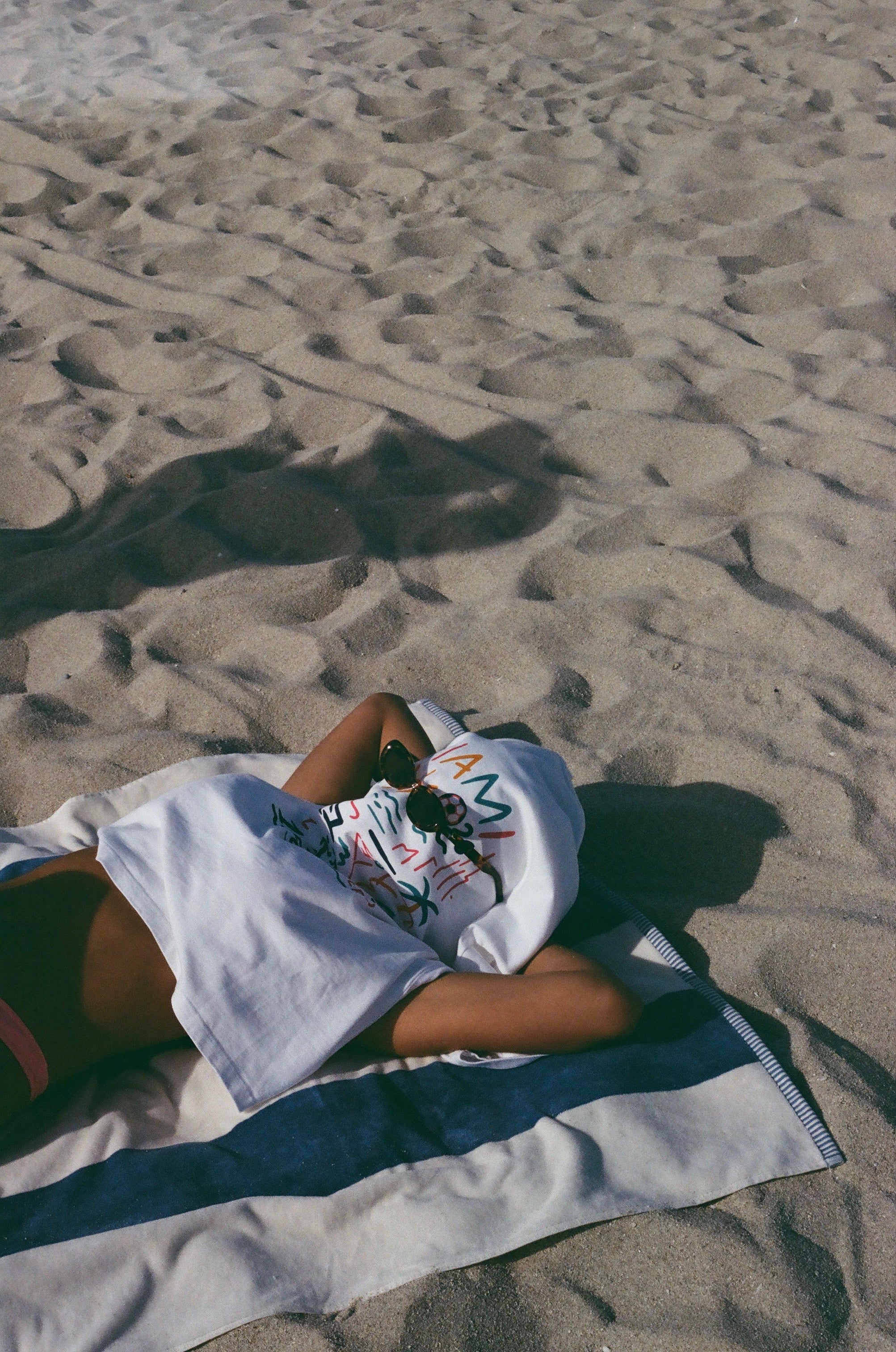 Model relaxing on the sand wearing the white Endless Summer graphic T-shirt