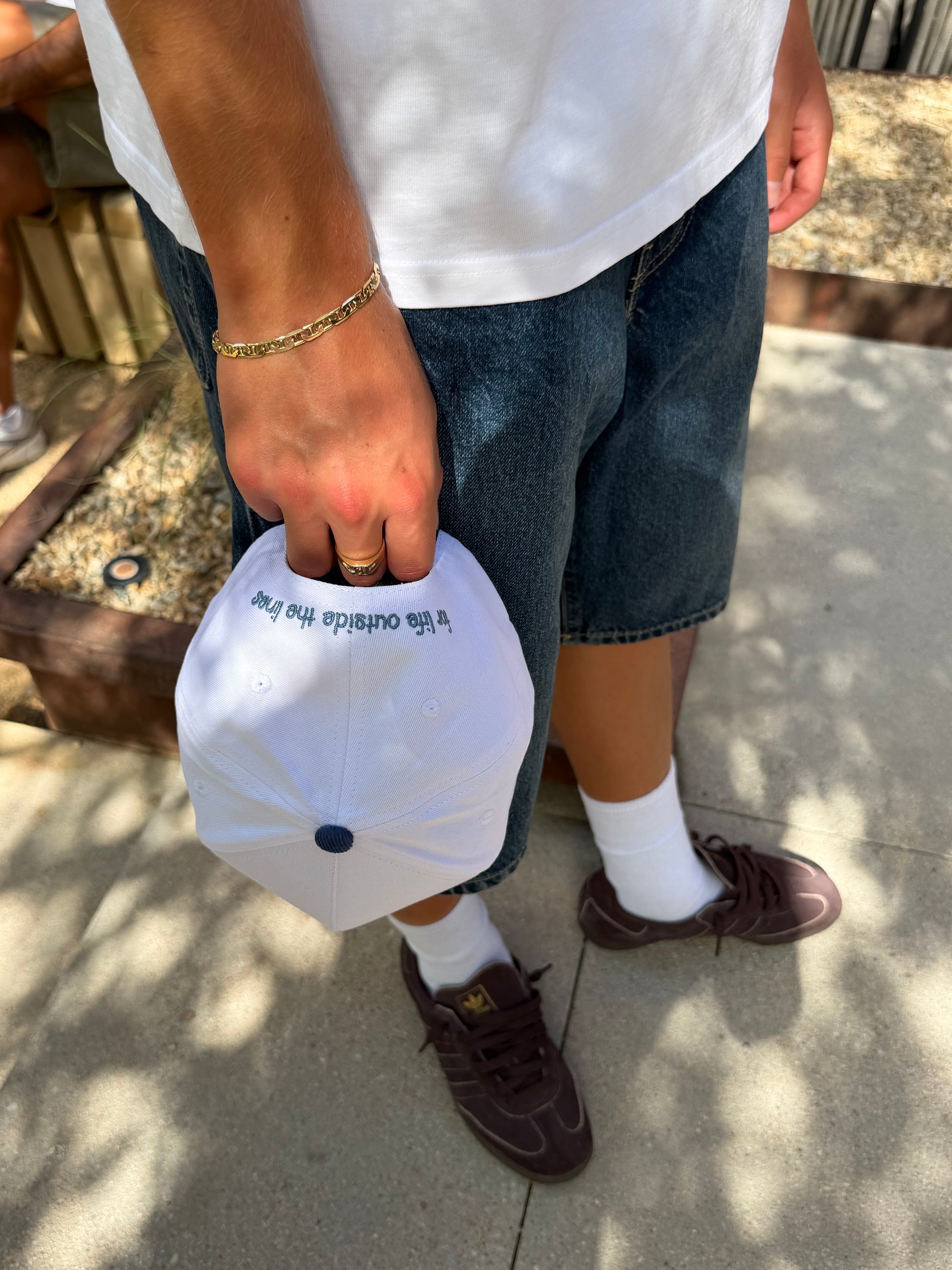 Person holding the white Endless Summer Hat, showing the embroidered “for life outside the lines” text on the back