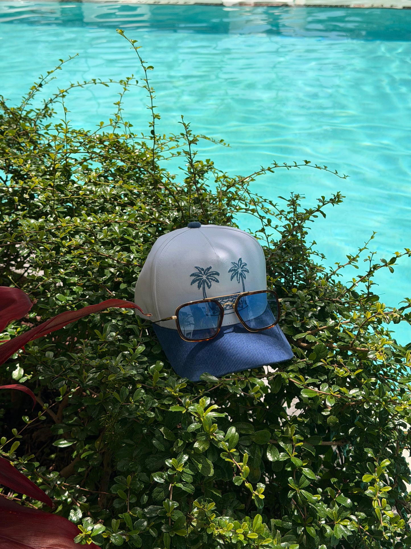 White Endless Summer Hat with navy corduroy brim and palm-tree soccer-goal embroidery beside a swimming pool