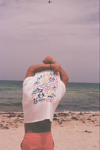 Model showing the colorful Miami-inspired back graphic of the white Endless Summer Tee at the beach